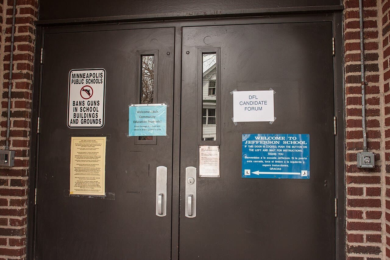 The entrance doors of the community school at 1200 West 26th Street in Minneapolis, posted with civic notices including a candidate forum.